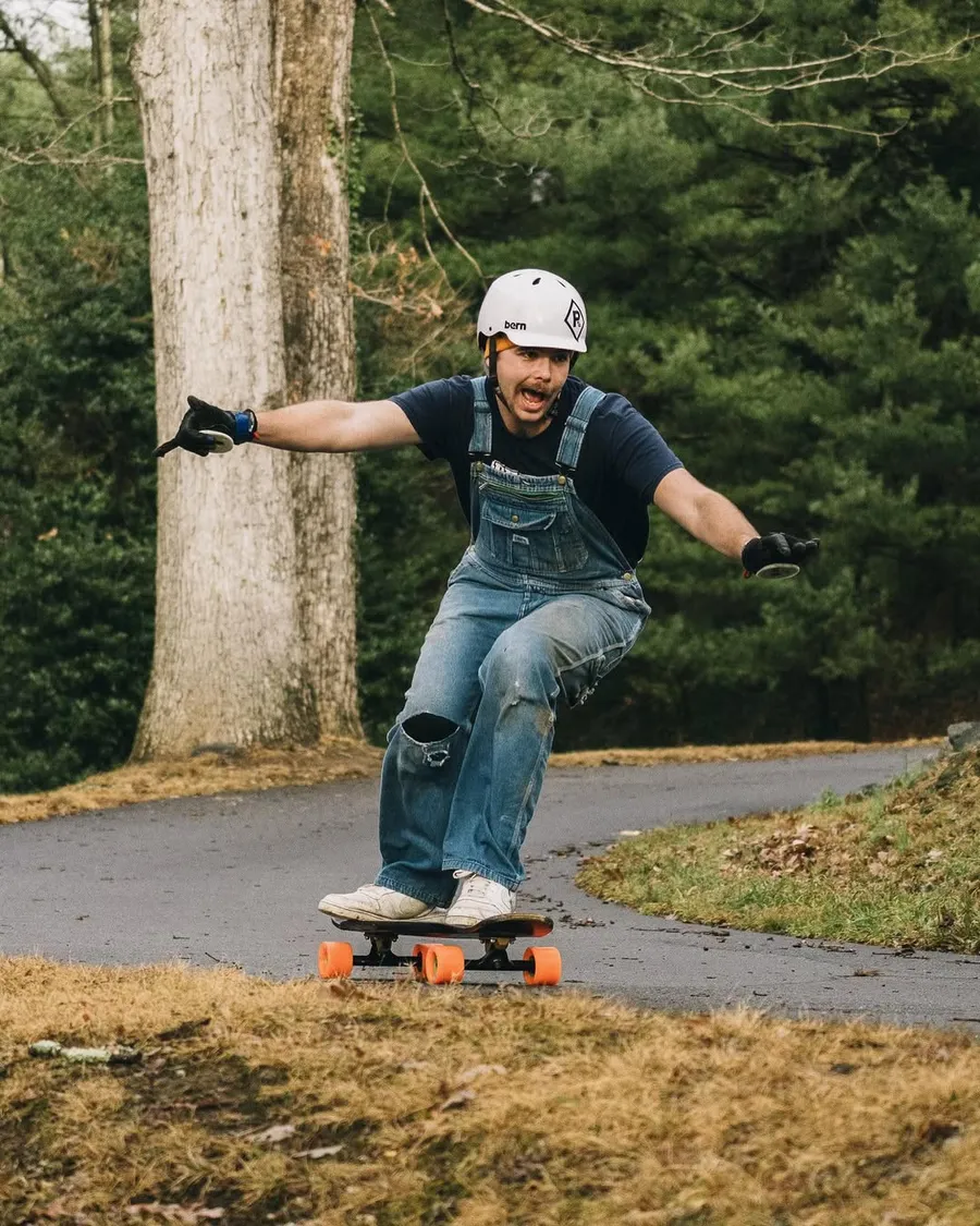 A man on a skateboard riding down a road wearing overalls and a helmet.