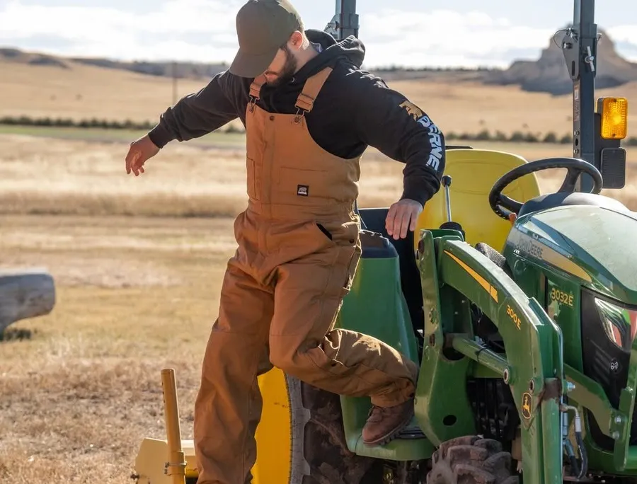 A coming down from a truck wearing insulated overalls.