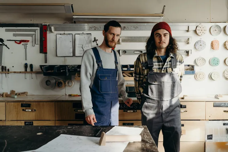 Two men wearing bib overalls standing at a wokshop