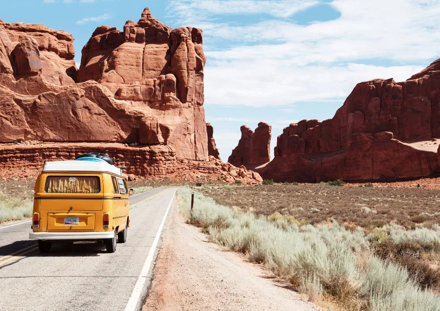 A yellow camper van driving towards red rock formations in Utah.