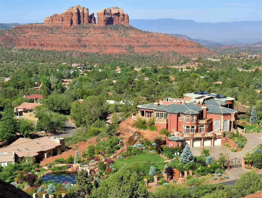 An aerial photo of the city of Sedona featuring greenery, buildings, a pond, and red rock formations in the background.