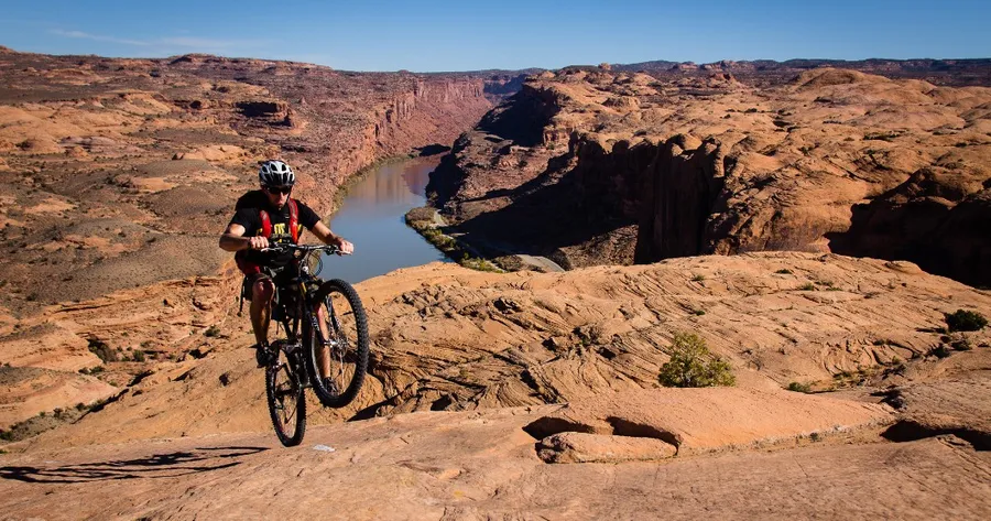 A cyclist doing a wheelie at Slickrock Bike Trail in Utah with the Colorado River in the background.