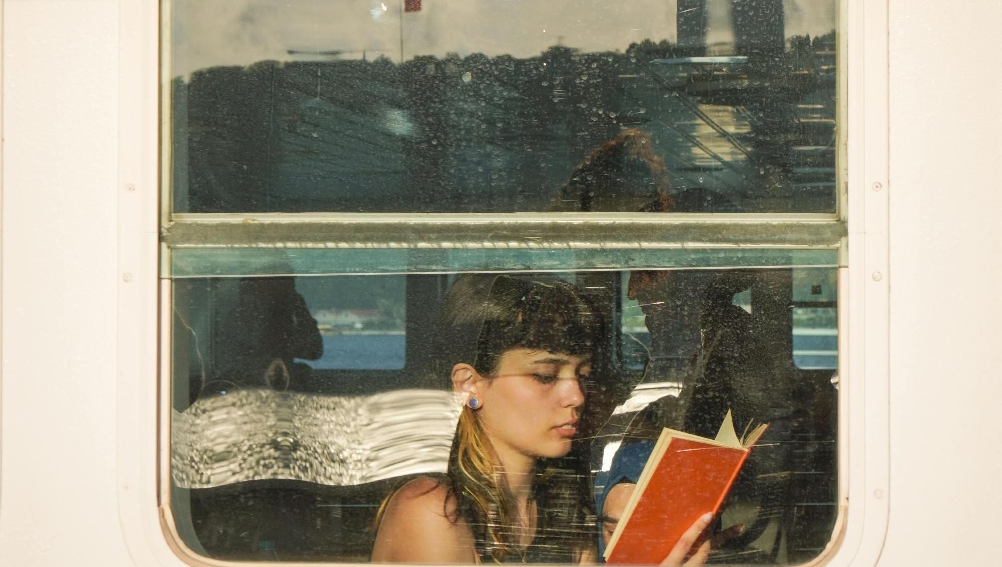 Solo female traveler with brown hair reading a red book by the window on a train during her trip.