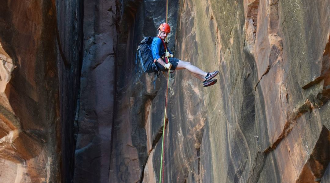 A man with shorts and a red helmet rappelling at the cliffs near Moab, Utah.