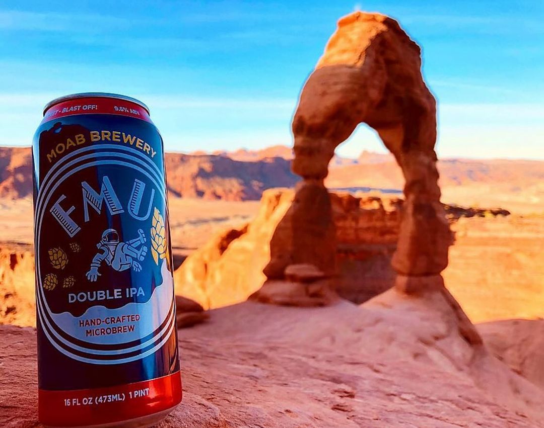 A picture of a can of an FMU Moab Brewery beverage near the delicate arch at Arches National Park.