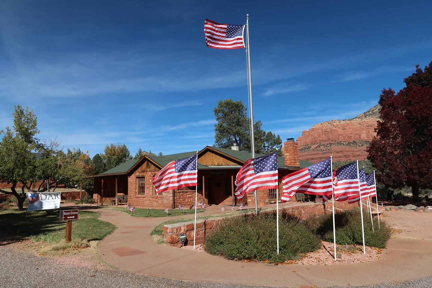 The Sedona Heritage Museum with American flags in the foreground and red rock formations in the background.